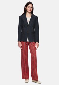 Navy blazer with gold buttons, contrasting stitching, and two front pockets, paired with red patterned wide-leg trousers. Casual shoes complete the look.