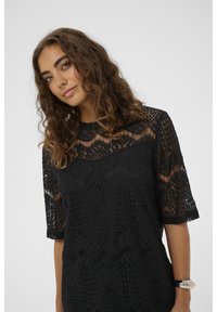 Fekete csipkés ruha rövid ujjakkal, bonyolult mintákkal és textúrákkal. Az dekoltázs félig áttetsző, részletes csipkebonyolítással.