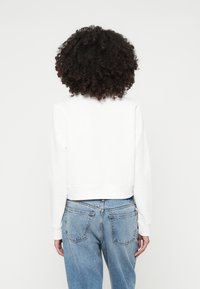 Κοντό λευκό φού�τερ από μαλακό υλικό, με ριμπ ύφανση στις μανσέτες και το στρίφωμα. Συνδυάζεται με ανοιχτό μπλε ψηλόμεσες τζιν παντελόνες.