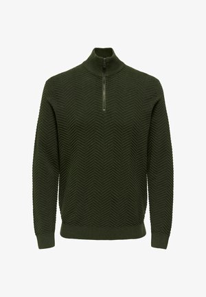 Tamsiai žalia megztinis su aukštu apykakle, turintis ketvirtinio užtrauktuko uždarymą. Audinyje išsiskiria tekstūruota chevrono raštas. Guminiai rankogaliai ir apačia.