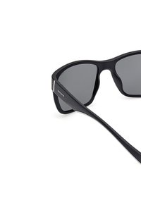 Gafas de sol negras con lentes grises, diseño de montura angular, superficie mate y detalle de logo plateado en la patilla. Construcción de plástico ligero.