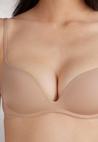 Nude Push-up-BH mit glatten, konturierten Cups, verstellbaren Trägern und einem tiefen Ausschnitt. Dezenter Glanz mit nahtlosem Design.