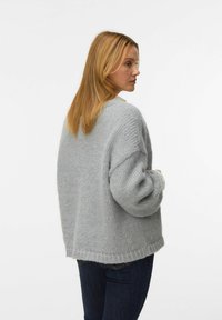 Suéter gris de gran tamaño de punto con acabado texturizado, cuello redondo y hombros caídos, combinado con jeans oscuros.