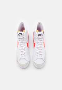 Scarpe Nike high-top in pelle bianca con swoosh rosso, punta grigia e dettagli giallo chiaro. Presentano lacci bianchi e un collo imbottito.