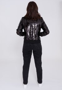 Czarna bomberka z cekinami, dopasowana w talii, z długimi rękawami, zestawiona z czarnymi dżinsami o wysokim stanie i białymi trampkami.