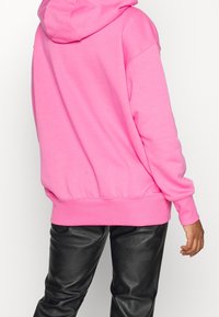 Pink hoodie with a front pocket, ribbed cuffs and hem, crafted from soft fabric. Worn with black faux leather pants.