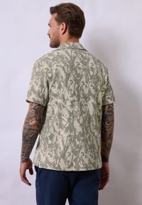 Kortärmad skjorta i ljusgrön med ett texturerat, abstrakt mönster. Har krage och en avslappnad passform, med rundad nederkant och sidoritsar.