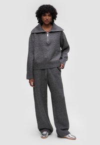 Szara dzianinowa sweter z dużym kołnierzem i zamkiem błyskawicznym do połowy, w połączeniu z pasującymi spodniami o szerokich nogawkach. Oba elementy wykonane są z miękkiego, strukturalnego materiału.