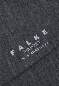 Mørkegrå sokker med et teksturert strikkemønster. Har hvit merkevaretekst "FALKE AIRPORT" og størrelsesdetaljer i hvitt garn.