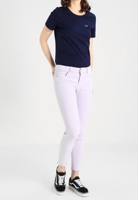 Camiseta de manga corta en azul marino, jeans rectos en lavanda y zapatillas negras con suelas blancas. La camiseta presenta un pequeño logo en el pecho.