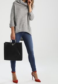 Szary sweter z dzianiny z kominem, niebieskie obcisłe dżinsy, czerwone szpilki i czarna torba na ramię z okrągłą rączką.