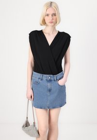Svart innpaknings-bodysuit kombinert med en lyseblå denim mini-skjørt. Skjørtet har en frontlomme og er komplementert med en sølvfarget håndveske.