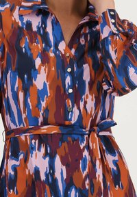 Kleurrijke, gemusterde jurk van lichtgewicht stof. Heeft een knoopsluiting aan de voorkant, een puntkraag en een strik ceintuur in een levendig kleurenpalet.