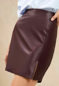Bordeaux leren miniskirt met een aansluitende vorm en een zijsplit. De gladde textuur en strakke lijnen benadrukken het moderne design.