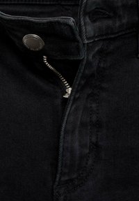 Black denim trousers feature a zip fly and button closure. The fabric is textured with a smooth finish and subtle stitching details.