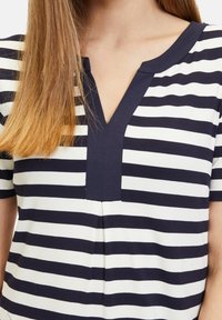 Navy and white striped top with a V-neck, short sleeves, and a gathered front detail, made from a soft, stretchy fabric.