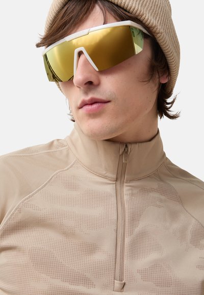 Beige zip-up athletic top with patterned texture; oversized sunglasses with gold lenses and white frame; beige knit beanie.