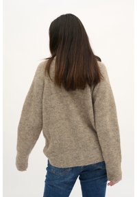 Maglione beige lavorato a maglia con una vestibilità ampia e maniche lunghe, caratterizzato da una texture morbida. Abbinato a jeans blu, visto da dietro.