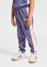 Lilla joggingbukser med en lyserød sideliste, elastisk talje og logodetalje. Bær med hvide sko med sorte accenter og gumisål.