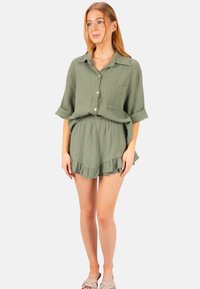 Chemise verte à boutons et short à volants assorti en tissu léger. Dotée d'une poche poitrine et de manches retroussées.