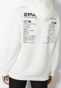Sudadera blanca con un gran estampado gráfico en la parte posterior que incluye títulos de canciones y el nombre del artista en texto negro. Puños y dobladillo acanalados.