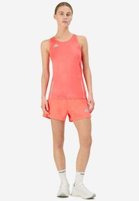 Canottiera sportiva rosa e pantaloni corti con logo Kappa. Il materiale sembra elastico. Gli accessori includono calzini bianchi e scarpe da ginnastica.
