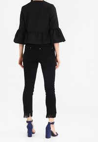 Zwart textuur top met uitlopende mouwen, gecombineerd met zwarte skinny broeken met franjes aan de onderkant en blauwe hoge hakken.