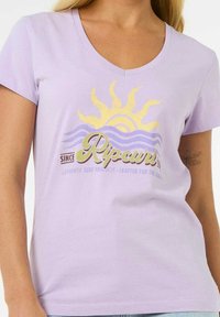 Lilla bomulds t-shirt med v-hals, der har et grafik med sol og bølger i guld og blå, samt "Ripcurl" tekst i grøn. Casual pasform.