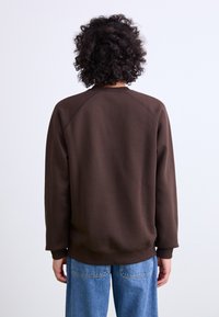 Brown, crewneck sweatshirt with raglan sleeves. Soft texture, ribbed cuffs and hem. Worn with light blue wide-leg jeans.
