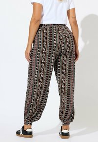 Zwarte joggerbroeken met een patroon, voorzien van verticale strepen met bloem- en geometrische ontwerpen. Elastische boorden en een elastische tailleband zorgen voor extra comfort en een goede pasvorm.