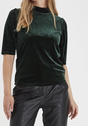 Tmavě zelený sametový top s krátkými rukávy, vysokým výstřihem a mírným nabíráním na ramenou, spárovaný s černými koženými kalhotami.