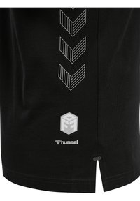 Svart träningströja med vita chevronränder och en logotyp vid fållen. Tyget verkar mjukt med en lätt textur, och det finns sidslitsar.