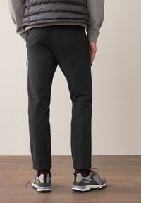 Pantalon noir avec poches zippées, associé à des chaussures grises et jaunes. Le tissu semble durable, avec une coupe détendue et un design fuselé.
