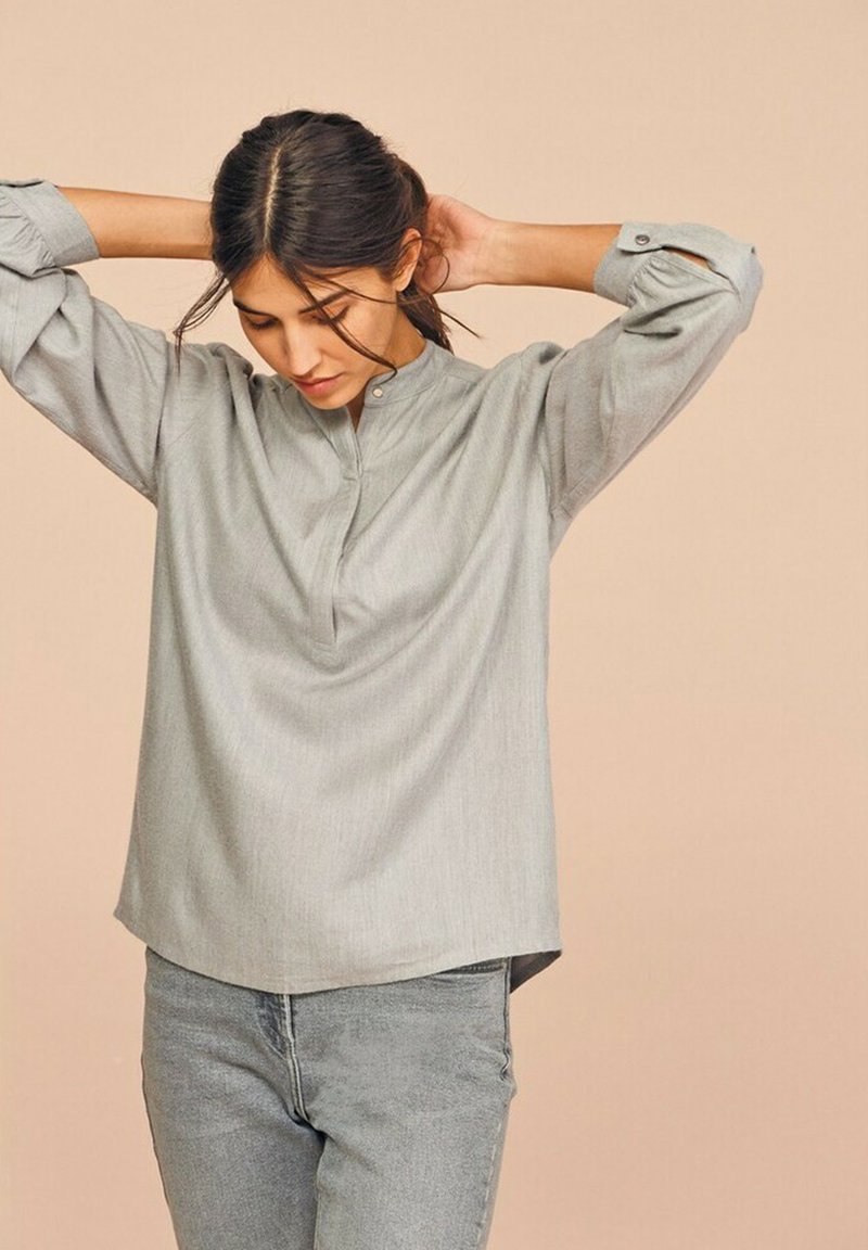 Lys grå langærmet skjorte med en mandarin krave, lavet af glat stof, der har et subtilt fald og opkrøllede ærmekanter, parret med lys grå jeans.