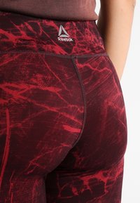 Leggings sportivi rossi con un motivo simile al marmo, vita alta e logo Reebok. Realizzati in materiale elastico con una texture liscia.