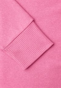 Gros plan sur un tissu tricoté rose montrant un poignet côtelé replié sur une section de manche lisse.