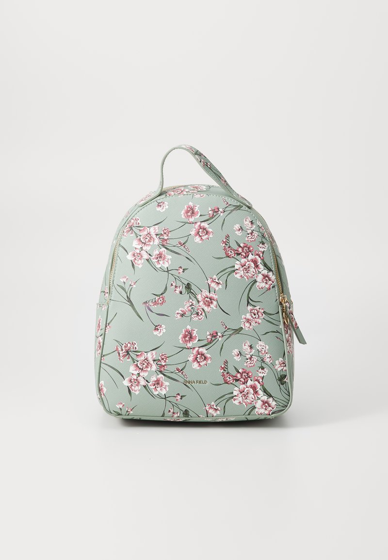 Mochila con estampado floral en verde menta. Presenta una forma redondeada, cremallera dorada y asa superior, adornada con flores rosas y blancas.