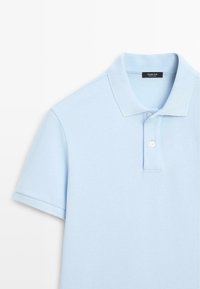 Hellblaues Polohemd mit kurzen Ärmeln, Kragen und zwei weißen Knöpfen, Etikett mit der Aufschrift Massimo Dutti, hergestellt in der Türkei.