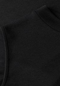 Gros plan sur un tissu noir montrant les détails de la manche et de la couture de l'épaule avec une texture fine et lisse en maille.