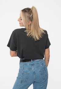 Black short-sleeve T-shirt made of soft cotton, paired with high-waisted blue denim jeans featuring back pockets and a black textured belt.