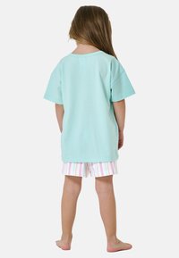 Camiseta de algodón azul claro con mangas cortas, combinada con pantalones cortos blancos que presentan rayas verticales en tonos pastel; vista desde la parte de atrás.