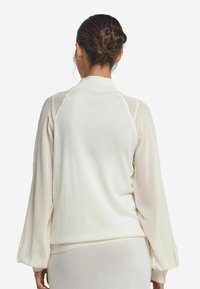 Maglione leggero in crema con maniche lunghe a palloncino; presenta un collo alto e una texture morbida; la vista posteriore evidenzia il tessuto liscio.