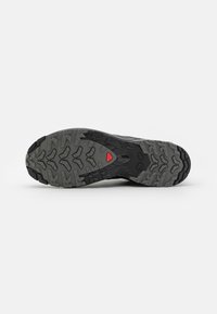 Black athletic shoe sole with a rugged tread pattern, featuring a grey and black color scheme and a red accent triangle at the center.