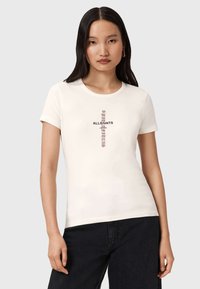 T-shirt en coton couleur crème avec des manches courtes, arborant un imprimé central en texte noir et maroon. Forme ajustée, col rond, design minimaliste.