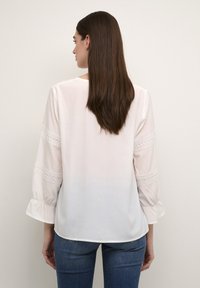 Blusa bianca con maniche a tre quarti, con dettagli in pizzo sulle maniche, in tessuto morbido e vestibilità comoda, abbinata a jeans blu.