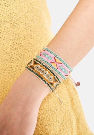Tre perlearmbånd på et håndled: et med pink og blå mønstre, et gyldent med geometriske designs og et andet med grønne perler.