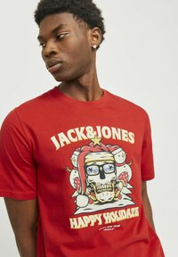 Camiseta de algodón roja con un diseño gráfico de un calavera con gafas y un sombrero de Santa, con el texto "JACK&JONES" y "HAPPY HOLIDAZE".