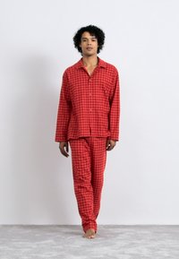 Red checked pajama set made of soft fabric, featuring a button-up shirt with a collar and loose-fitting pants. No visible patterns or accents.
