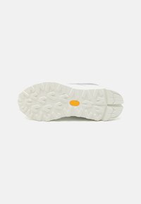 White sneaker sole featuring a textured rubber outsole with a jagged pattern and a yellow logo at the center.