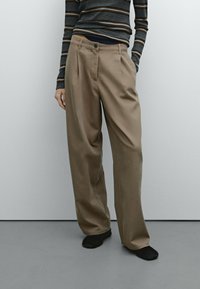 Szerokie, beżowe spodnie o fakturowanym wykończeniu, z przodem zapinanym na guzik oraz zaszewkami. Połączone z dopasowanym swetrem w paski.